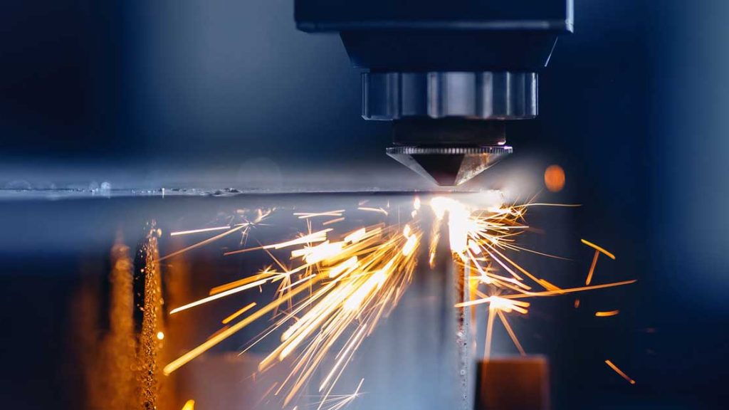 Eine Nahaufnahme einer Laserschneidemaschine, die Metall durchschneidet, wobei leuchtend orangefarbene Funken aus der Schnittstelle sprühen.