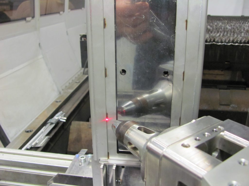 Ein Laserausrichtungsgerät projiziert einen roten Strahl auf eine Metalloberfläche, dessen Reflexion auf einer spiegelartigen Platte sichtbar ist, was eine präzise Einrichtung der Maschinen erleichtert.